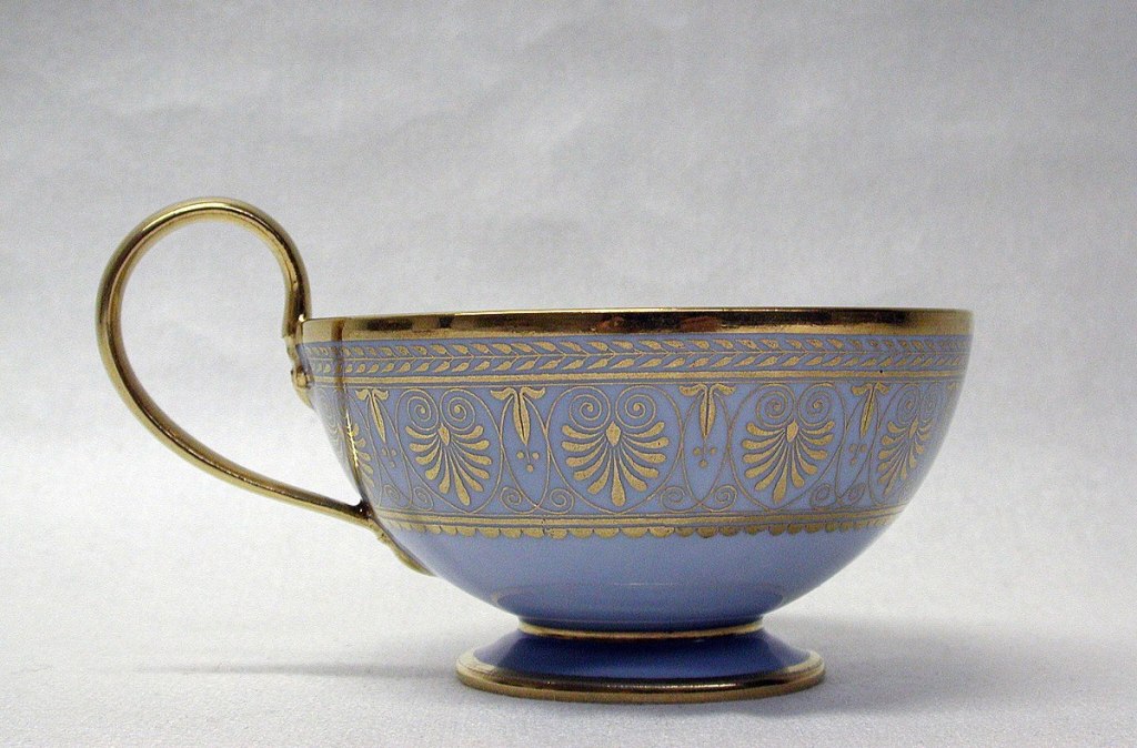 Gilded blue teacup with a golden handle. The pattern is reminiscent of palm leaves.